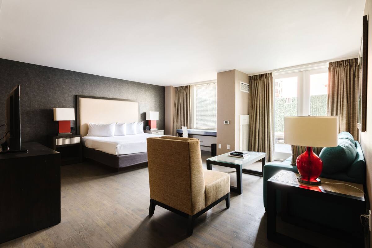 A hotel room with a bed, a chair, a desk, a red lamp, and a sofa.