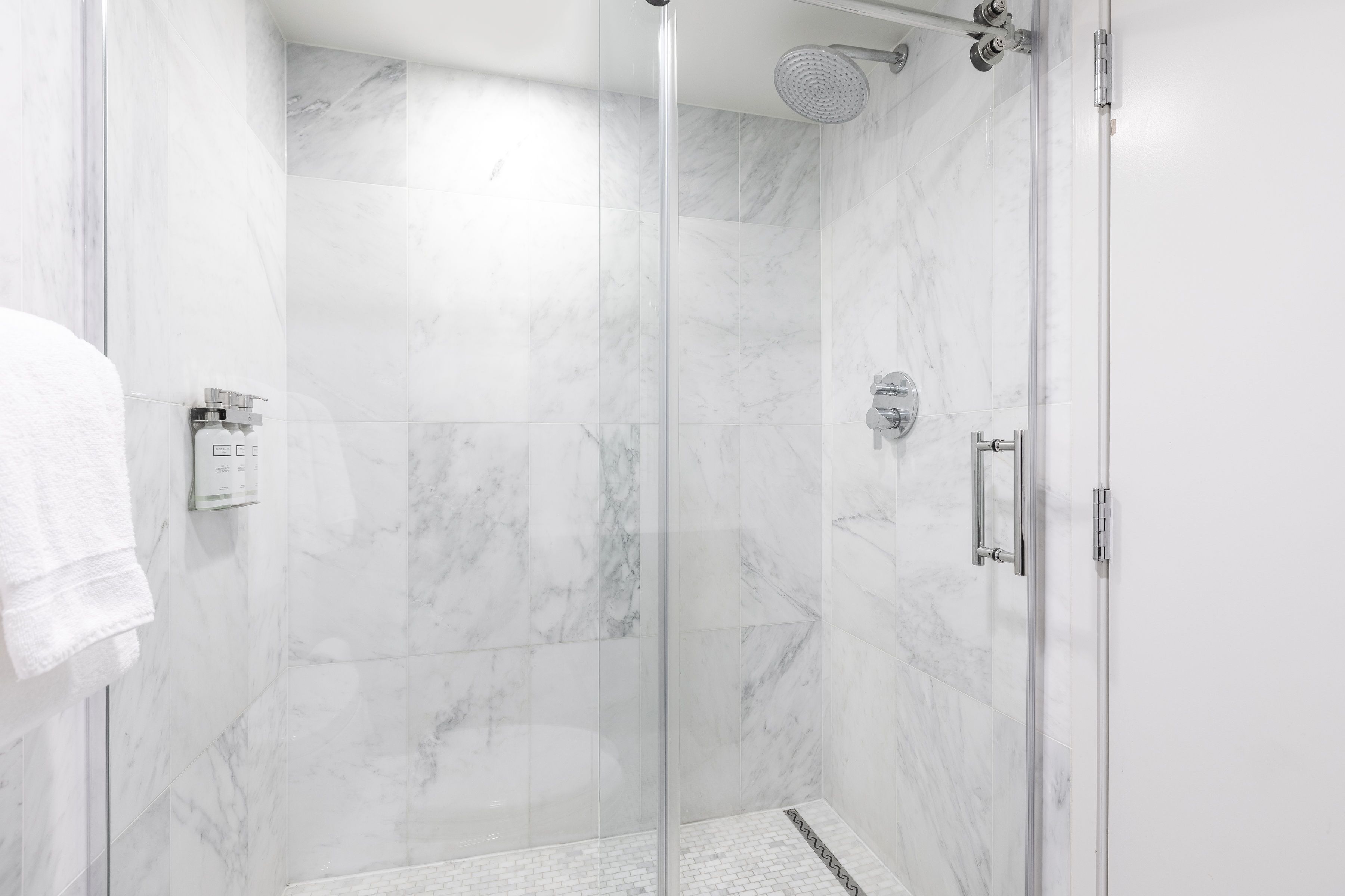 A glass-enclosed shower with a handheld showerhead and a wall-mounted control panel.