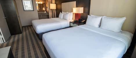 A hotel room with two beds, a desk, a chair, a wardrobe, a mirror, and a bathroom visible through an open door.