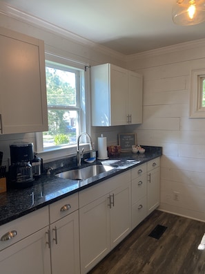 Enjoy a kitchen with a large window offering a view of the surrounding greenery, a sink, and a coffee maker.