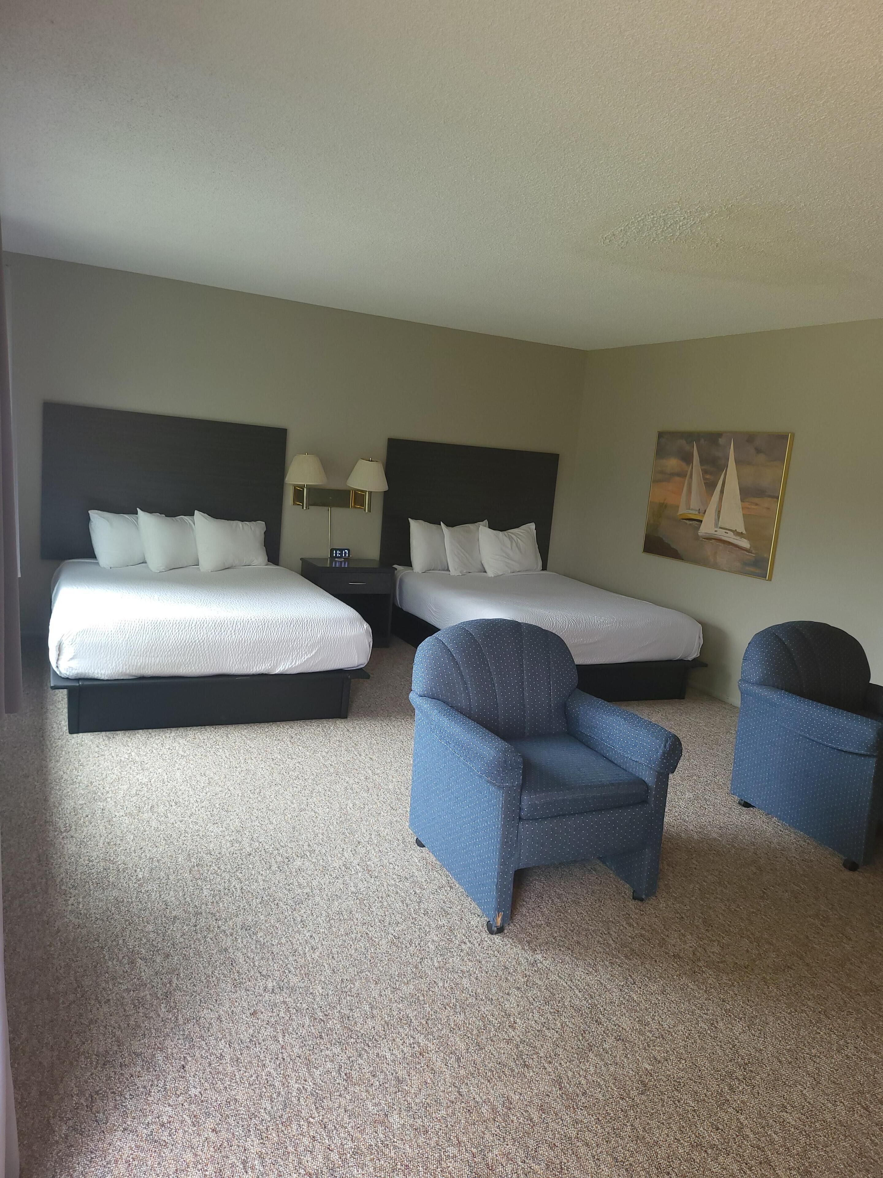 A hotel room with two beds, a chair, and a small table.