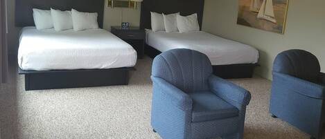 A hotel room with two beds, a chair, and a small table.