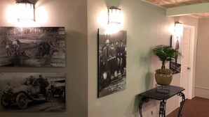 Un pasillo con fotografías en blanco y negro de estilo antiguo en las paredes, una planta en maceta sobre una mesa y una puerta al final.