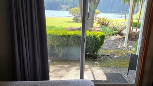 Una habitación con un amplio ventanal corredera que da a un balcón con vistas a un lago, vegetación y una cadena montañosa distante.