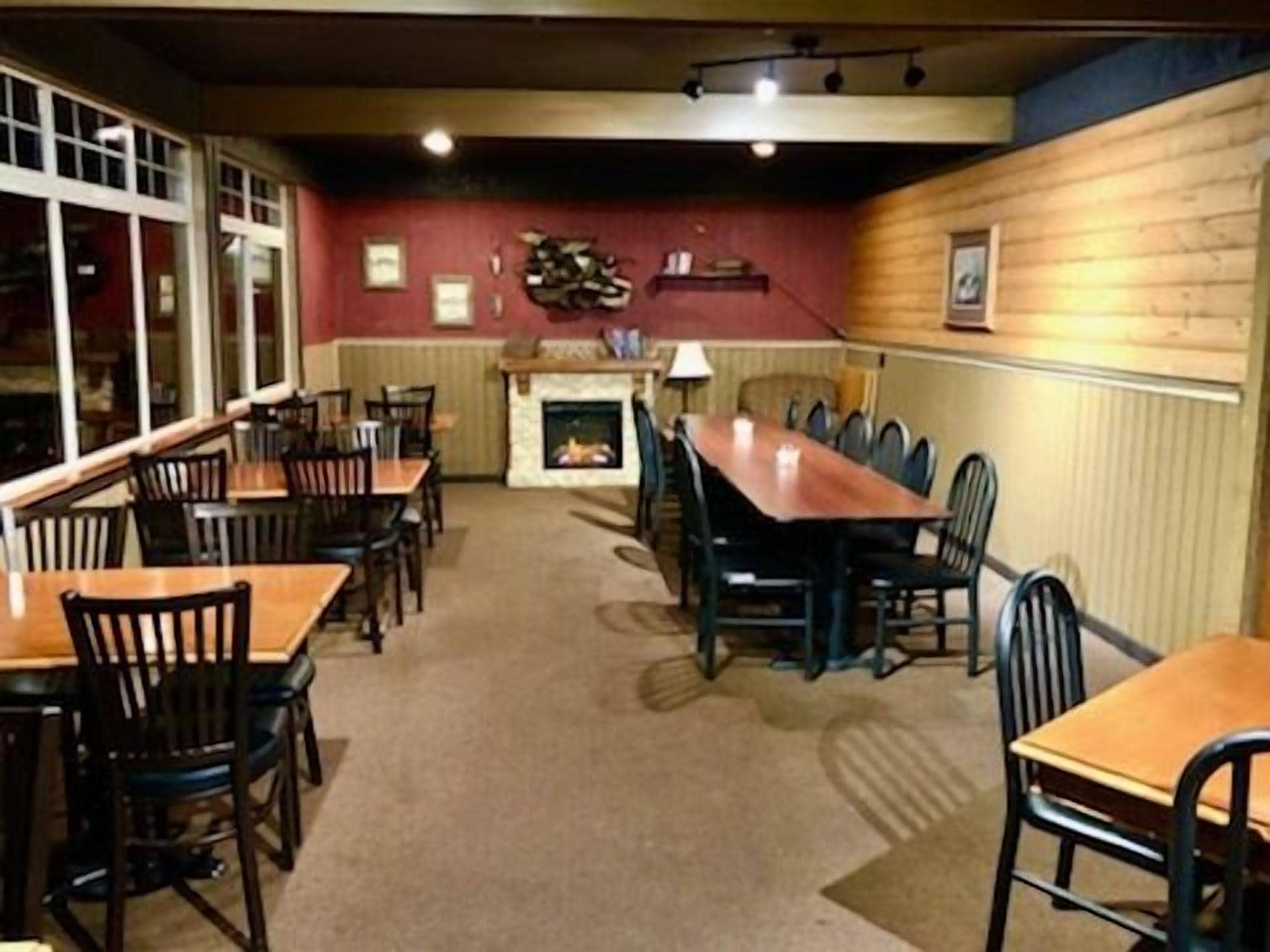 Un restaurant avec une longue table et des chaises en bois, une cheminée et un mur rouge orné de tableaux.