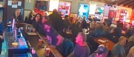 Un bar affollato con banconi in legno e clienti seduti ai tavoli.