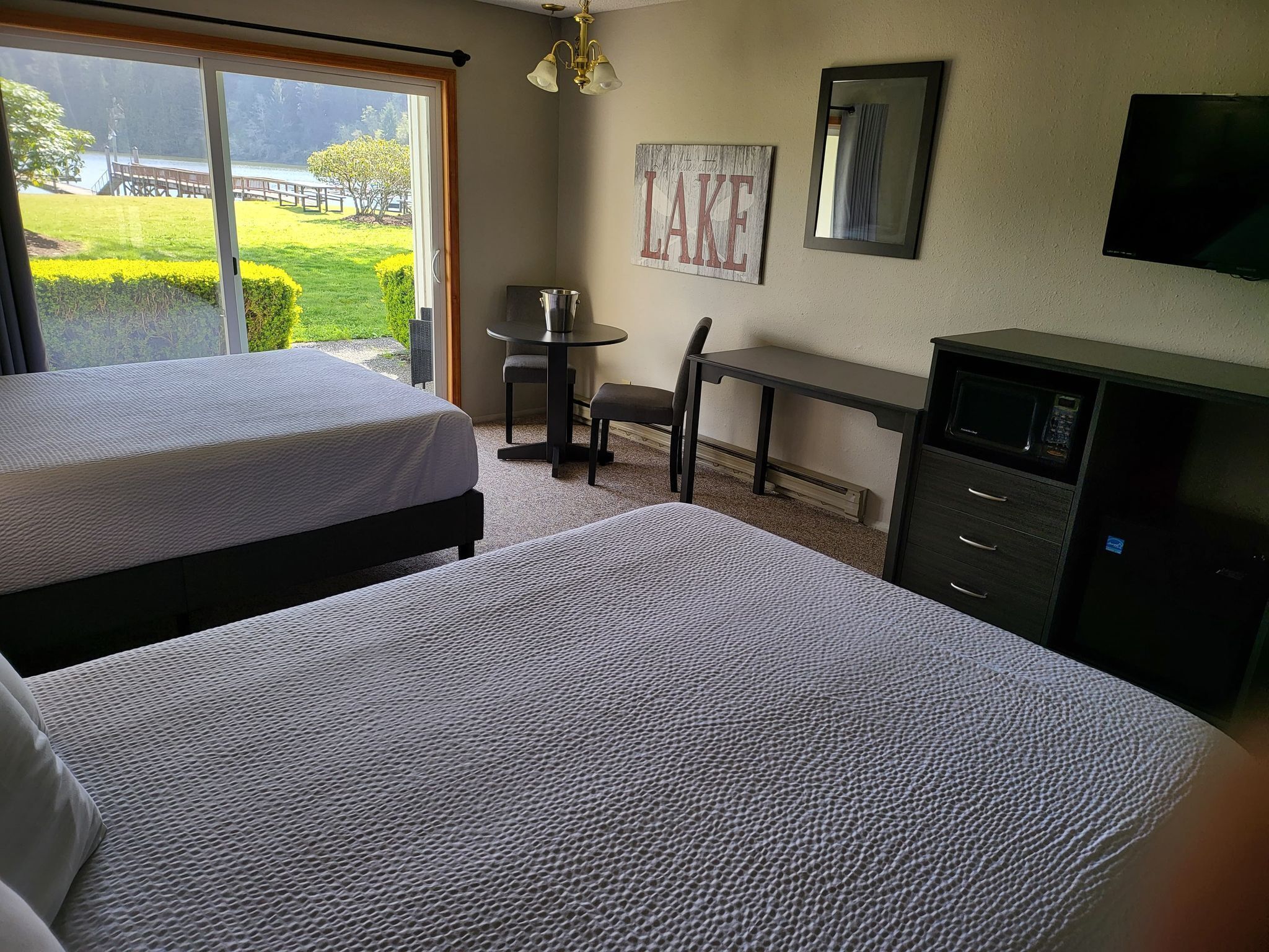 A hotel room with two beds, a desk, a chair, a TV, and a sign that says "LAKE".