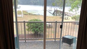 Una habitación con un amplio ventanal corredera que da a una terraza con vistas a un lago y colinas boscosas.