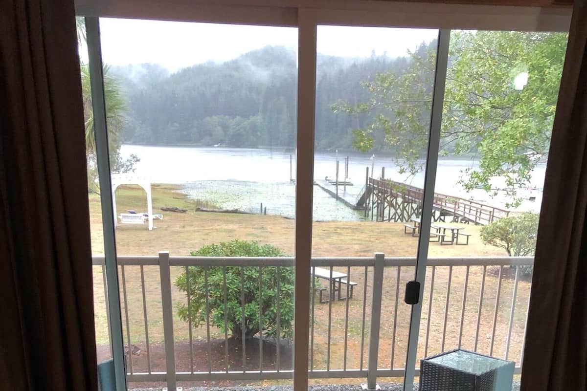 Ein Zimmer mit einer großen Schiebeglasdoor zum Deck mit Blick auf einen See und bewaldete Hügel.