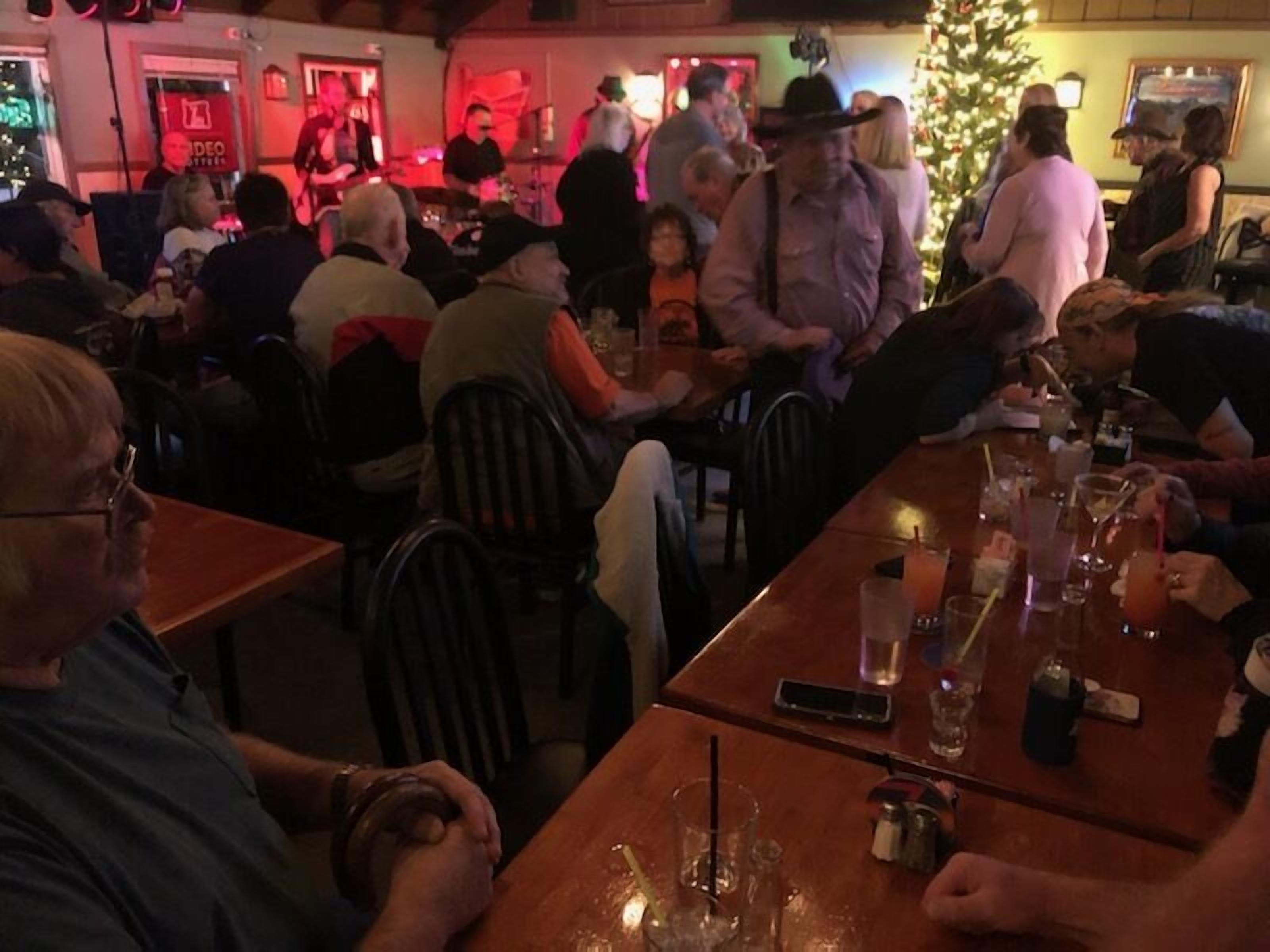 A crowded indoor venue with tables and chairs, a stage with performers, and a Christmas tree.
