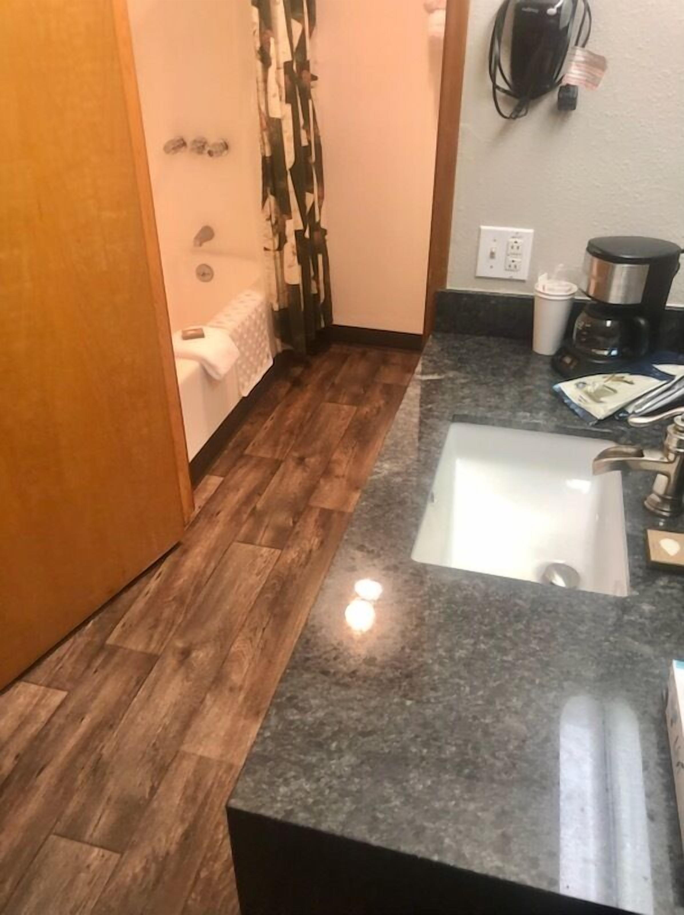 A small bathroom with a wooden floor, a sink, and a coffee maker.