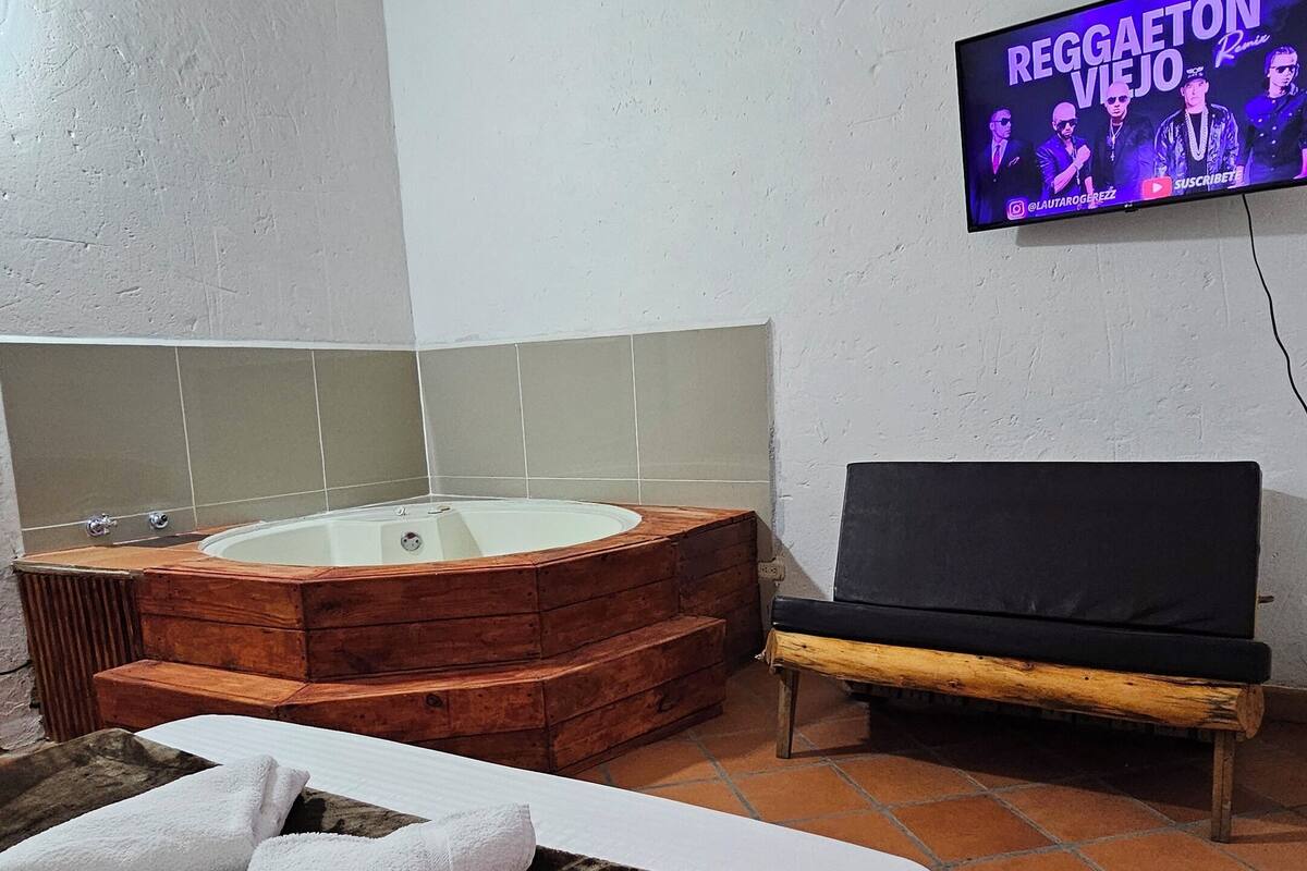 A room with a bed, a wooden hot tub, a television, and a tiled floor.