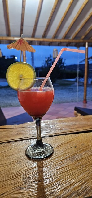 A cocktail in a glass with a straw and a lime slice on a wooden table. - Hostería Brisas del Río (Marinilla)