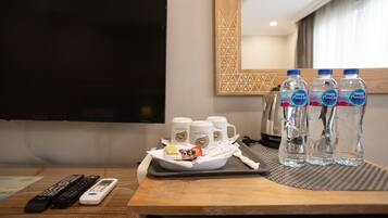 Habitación de hotel con televisor, controles remotos, una bandeja con botellas de agua y vasos, y otra bandeja con aperitivos.