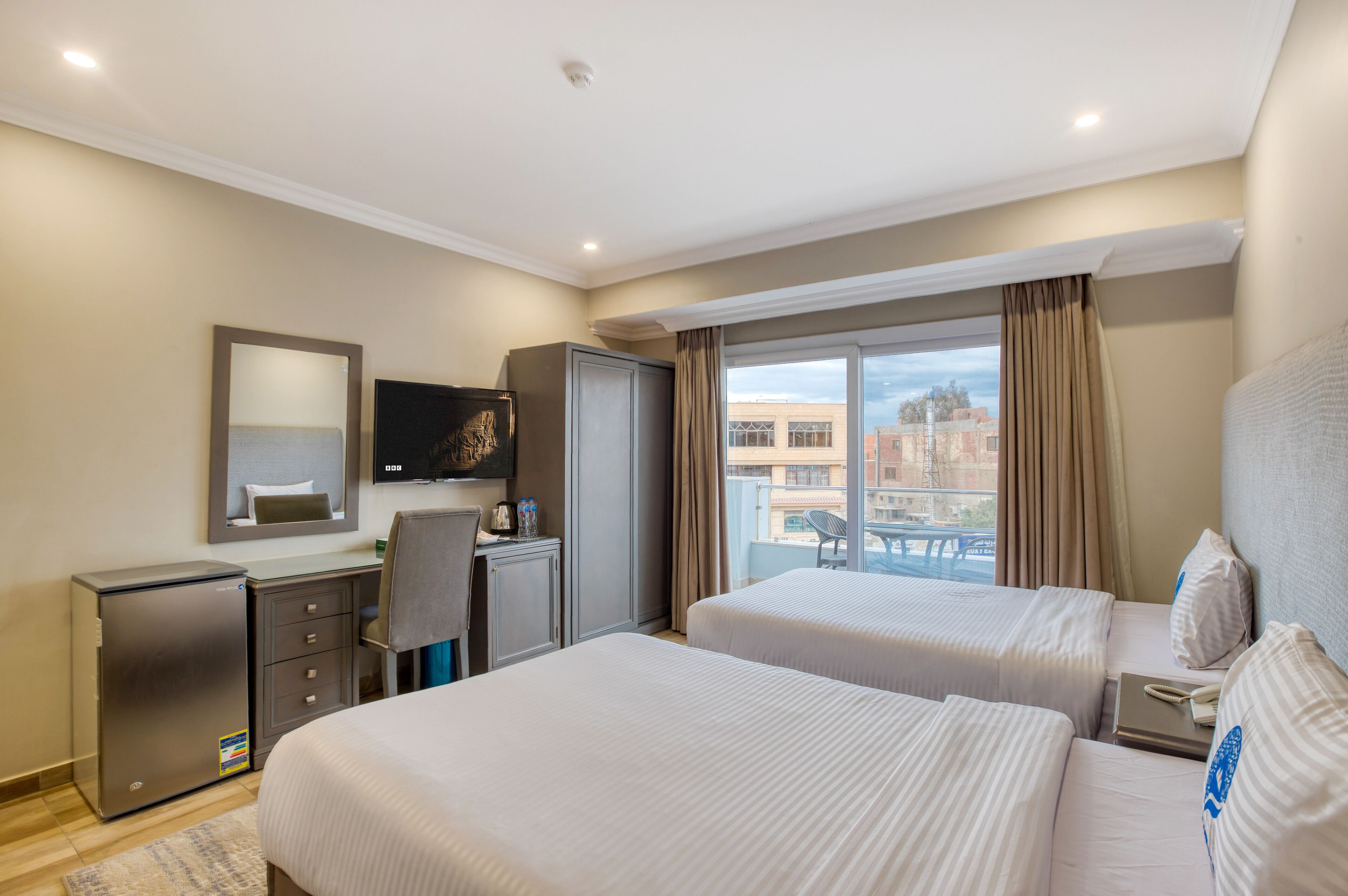Habitación de hotel con dos camas, un escritorio, un televisor y vistas a la ciudad.