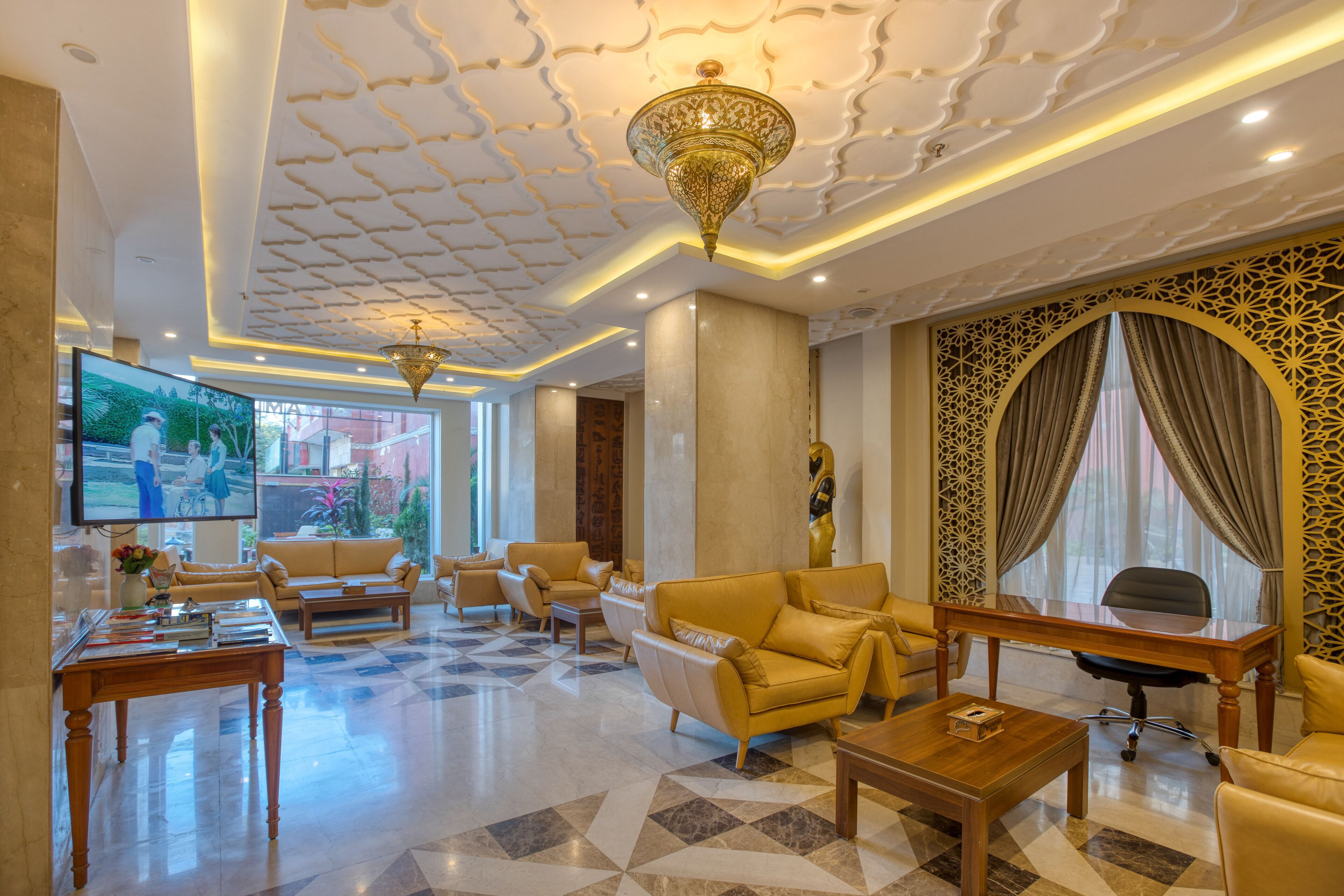 A spacious lobby with a large television, comfortable seating, a decorative ceiling, and a large window with curtains.