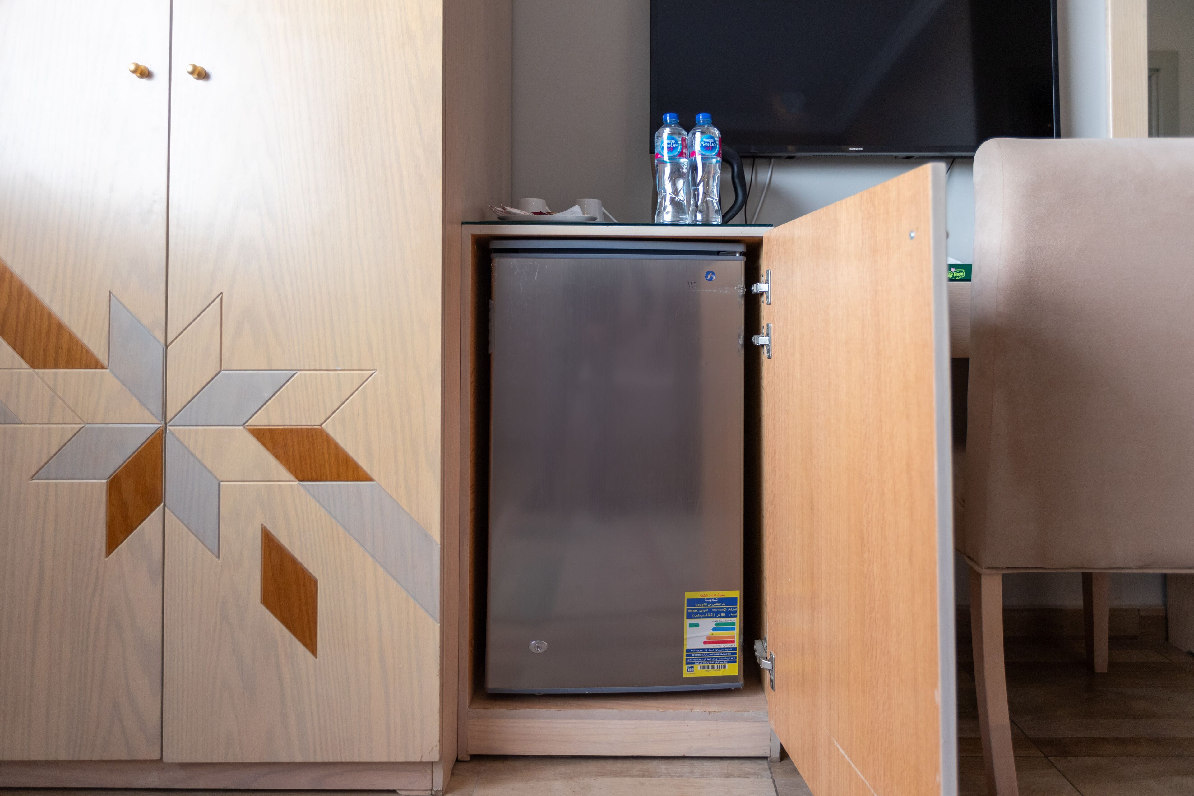 A compact minibar with a refrigerator, a flat-screen TV, and a seating area.