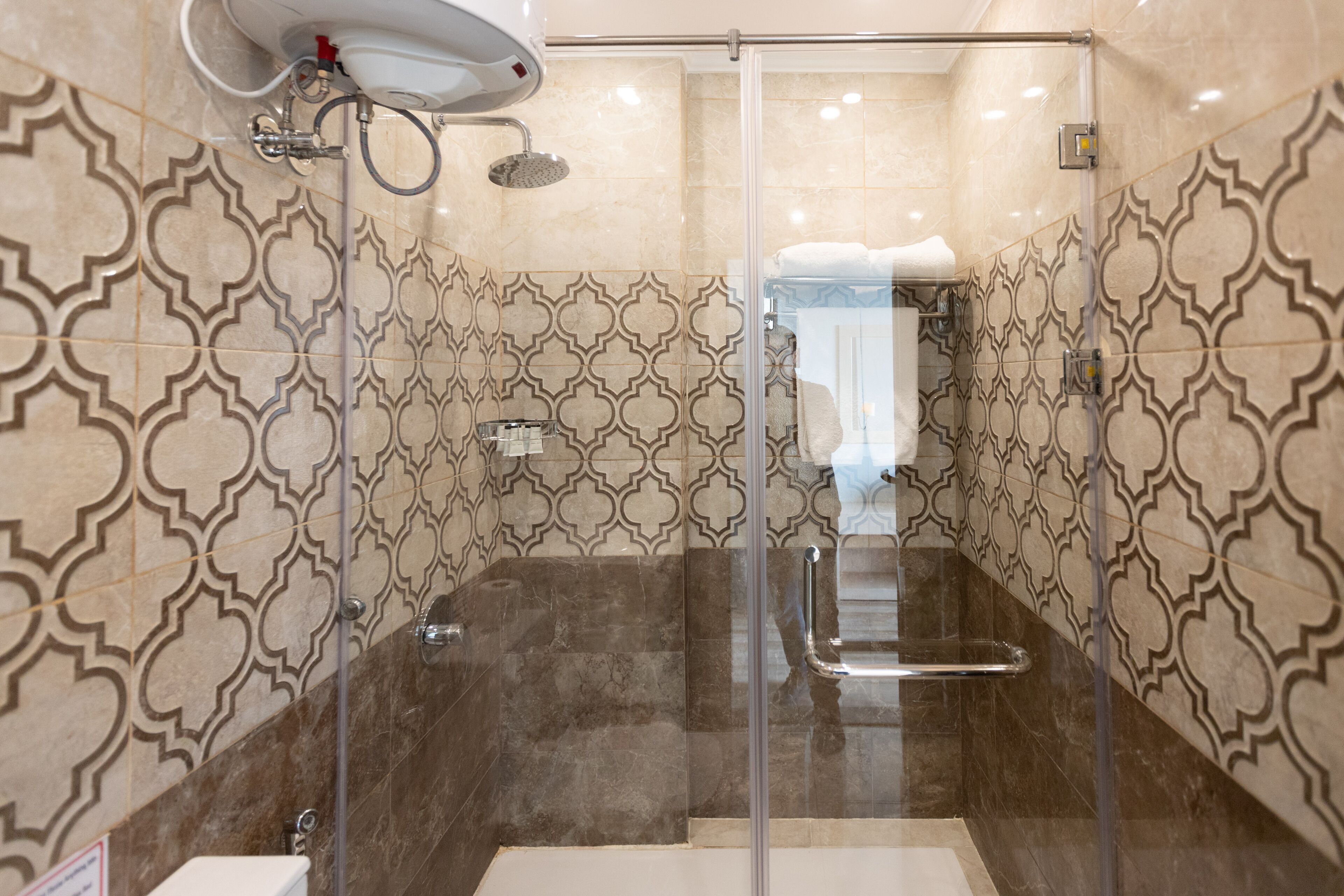 Un baño moderno con cabina de ducha de vidrio, azulejos estampados y un perchero visible.