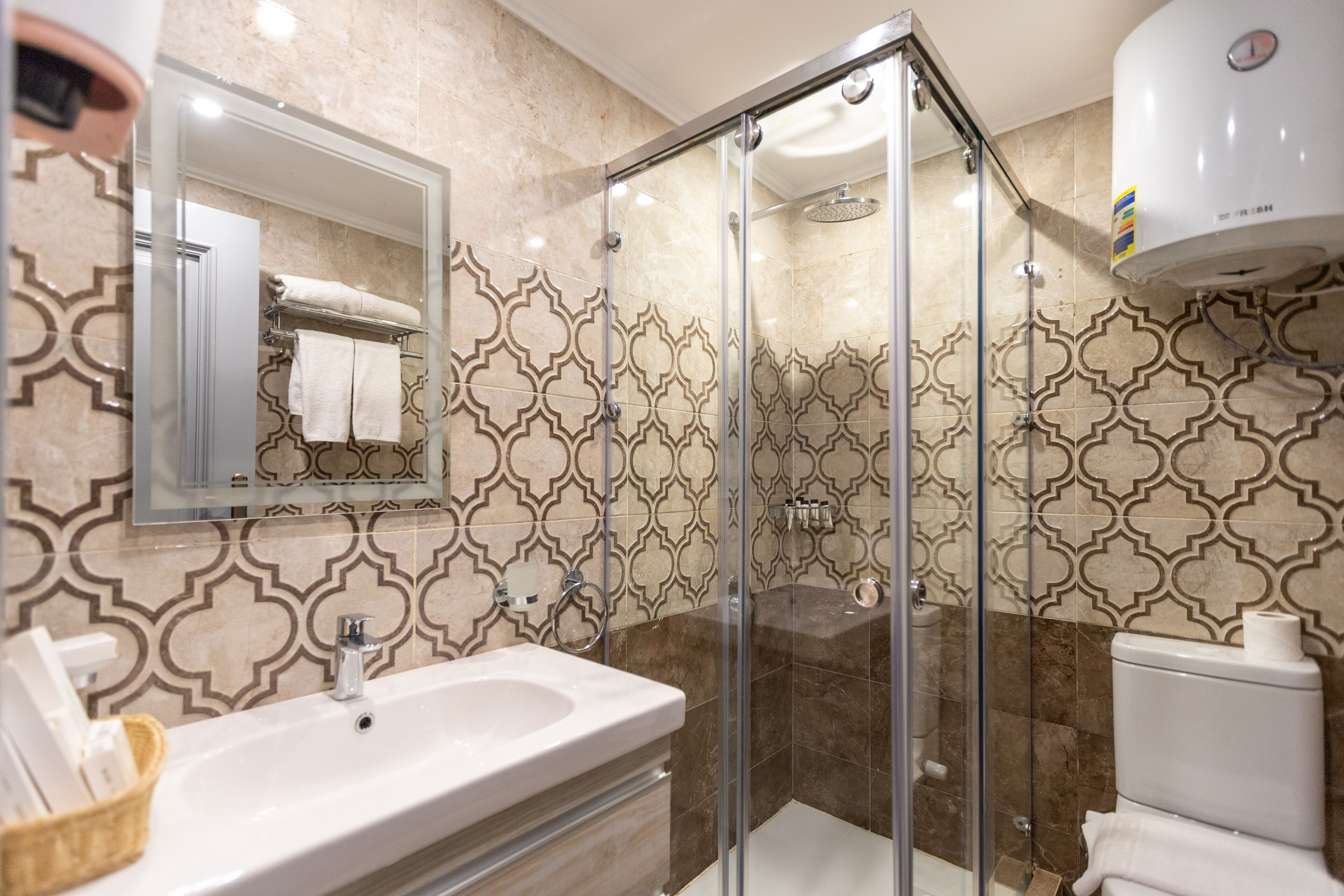 Un bagno moderno con doccia vetrata, lavandino bianco e pareti rivestite di piastrelle decorate.