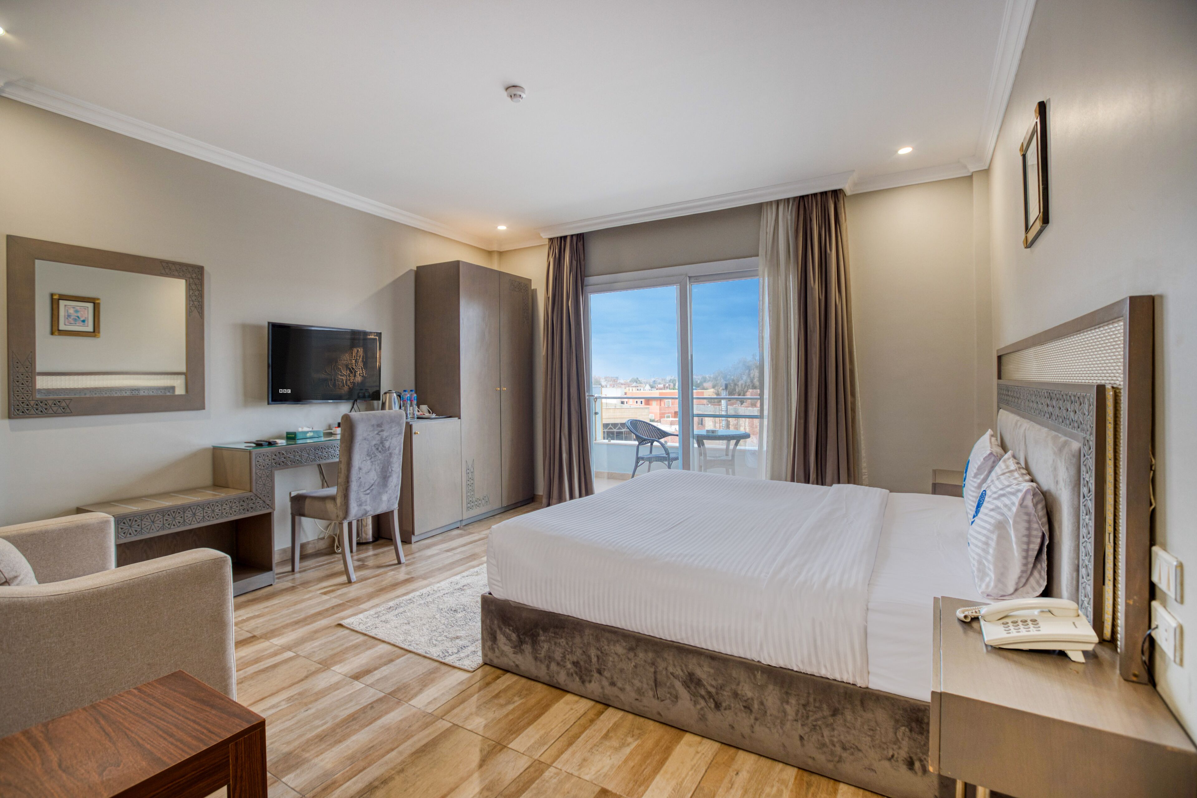 Une chambre d’hôtel avec un grand lit, un bureau avec une chaise, une télévision et une vue sur la ville par la fenêtre.