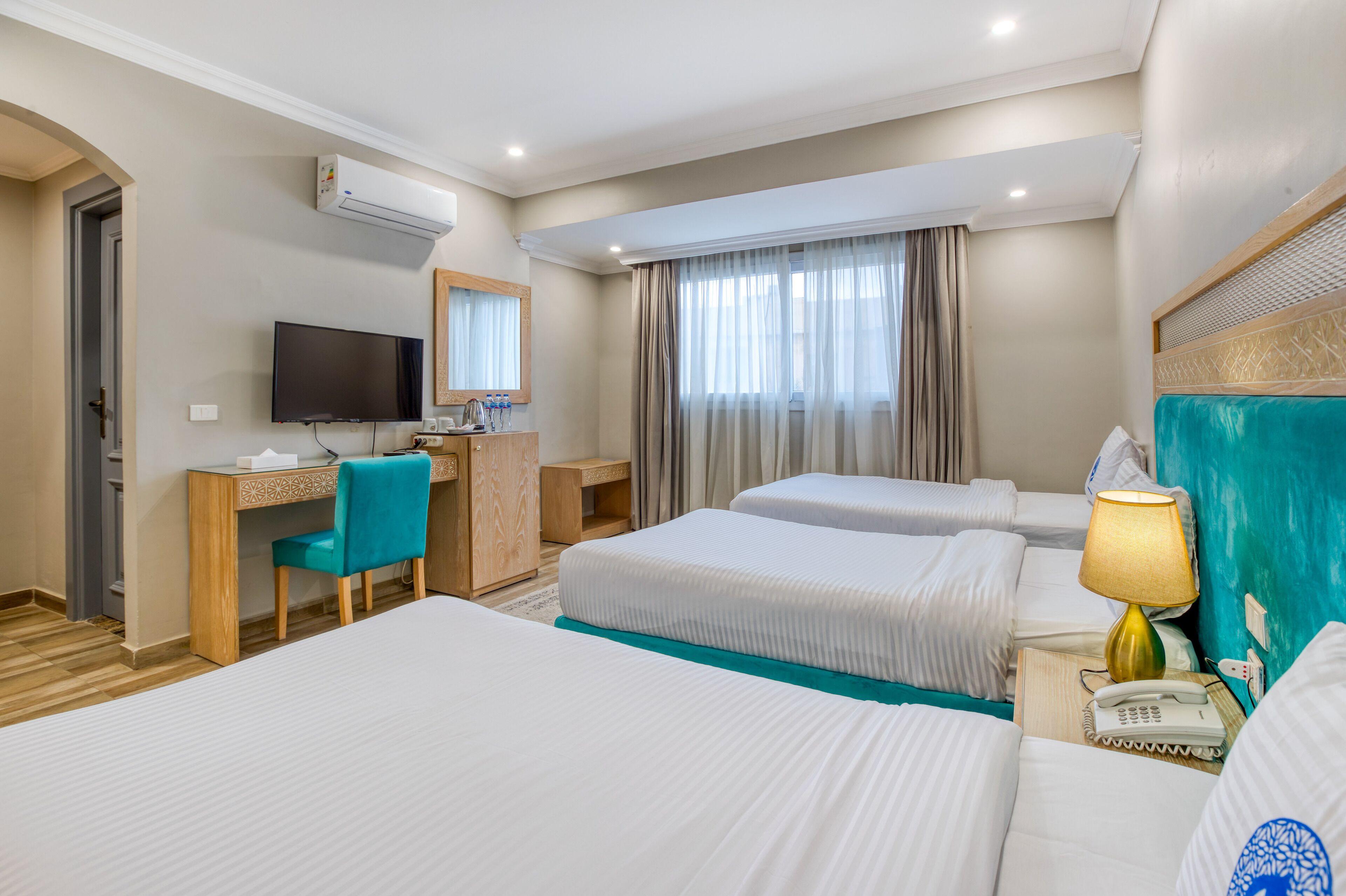 A hotel room with two beds, a desk with a chair, a television, a telephone, and a window with curtains.