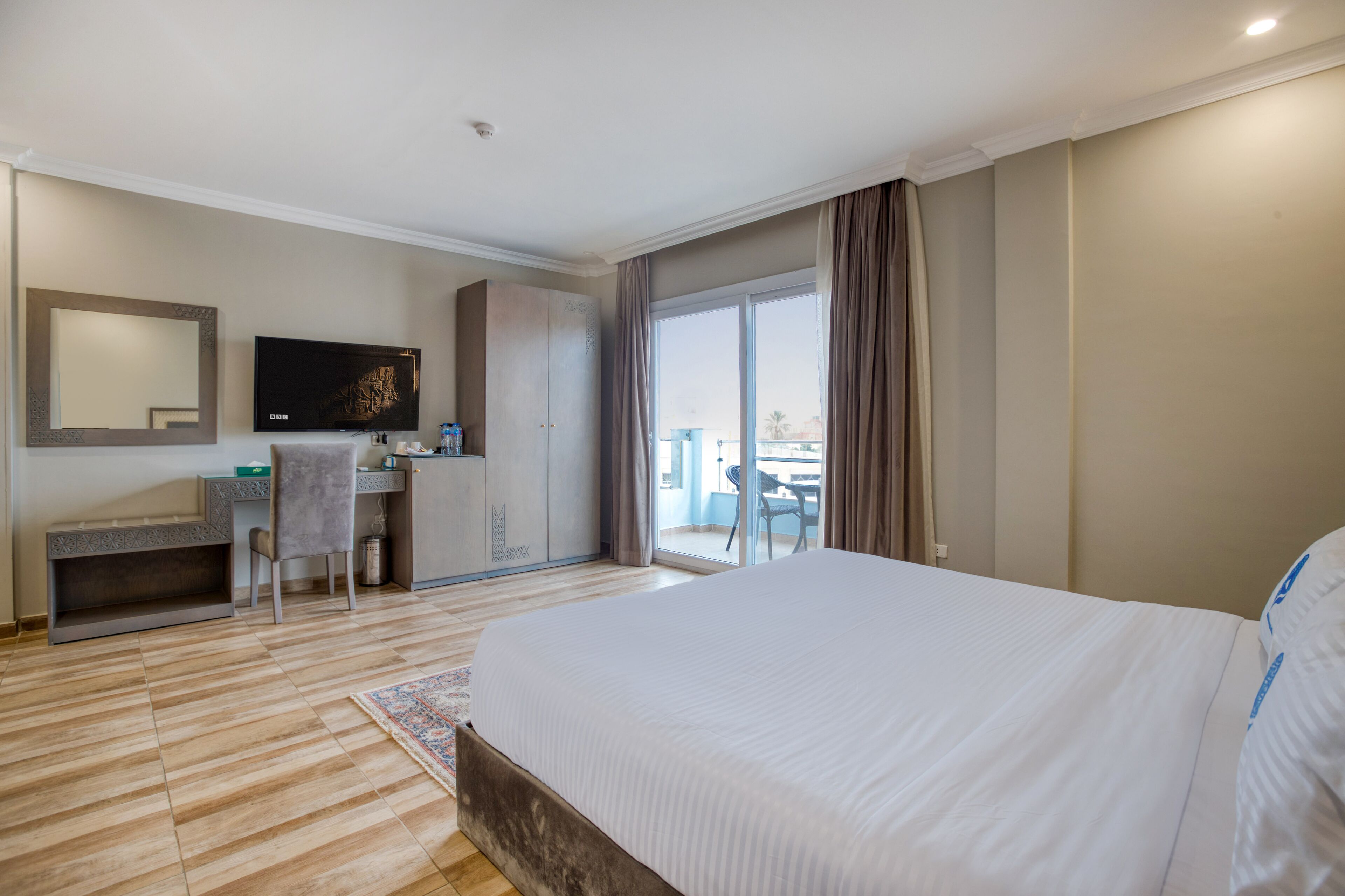 Habitación de hotel con una cama grande, un escritorio con silla, televisión y balcón con vistas.