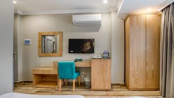 Habitación de hotel con cama, escritorio con silla, televisor, armario y aire acondicionado.