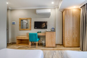 Habitación de hotel con cama, escritorio con silla, televisor, armario y aire acondicionado.