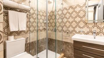 A bathroom with a glass-enclosed shower, a white toilet, a sink with a mirror, and patterned tiles.