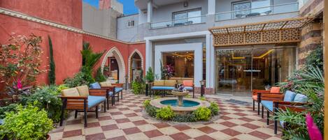 A courtyard with checkered flooring, outdoor seating, a fountain, and lush greenery.
