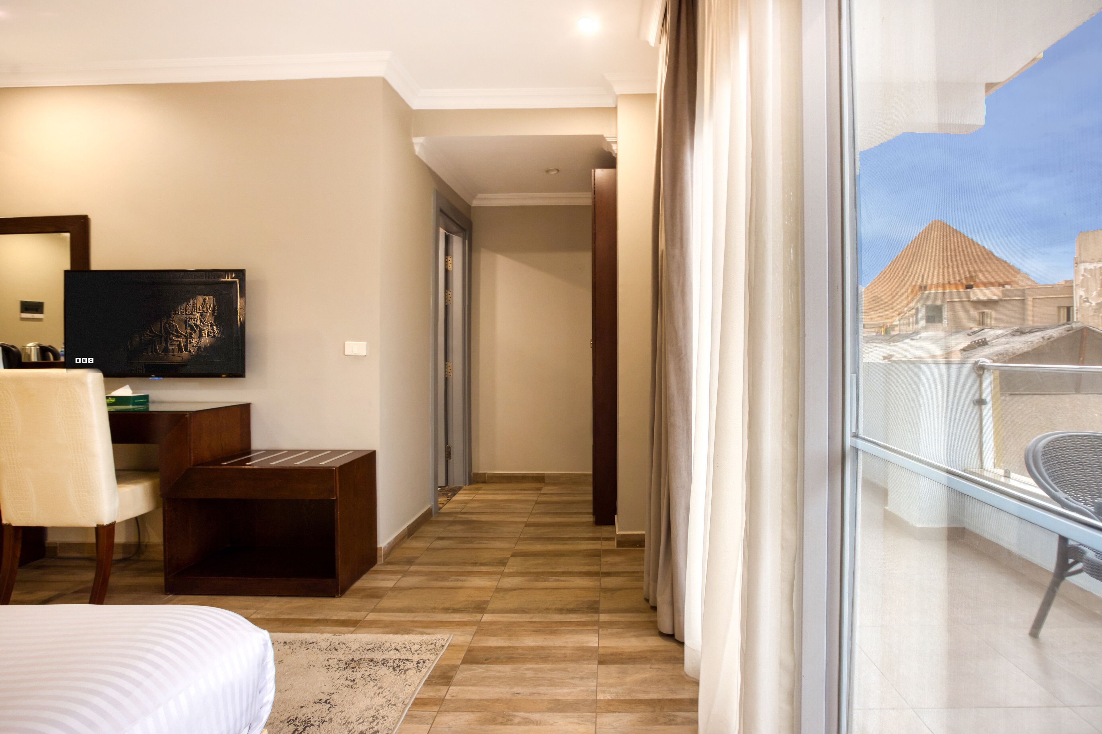 Une chambre d’hôtel avec un lit, un bureau, une chaise, une télévision et une vue sur les pyramides.
