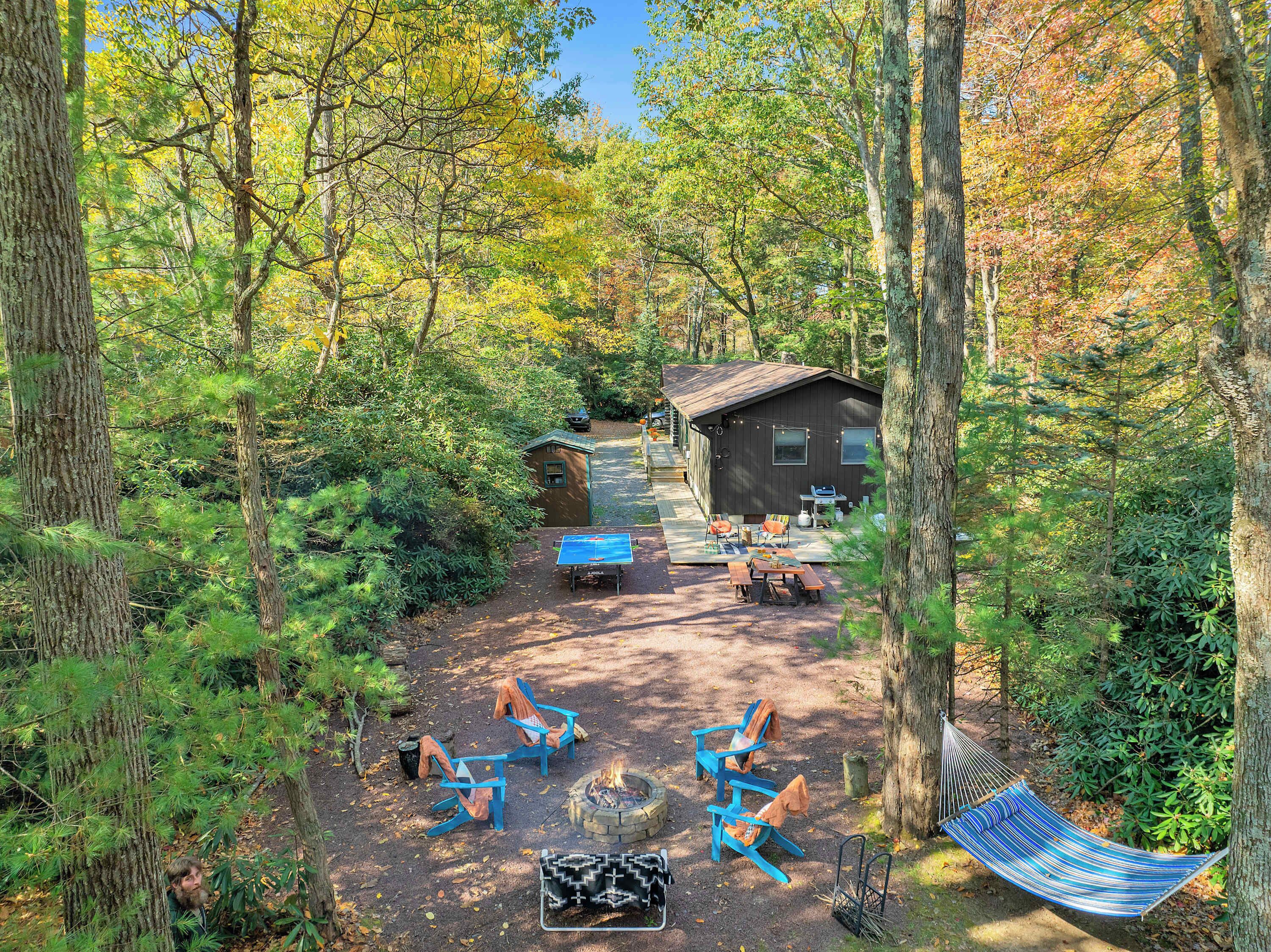 A cabin surrounded by trees, with outdoor seating and a fire pit.