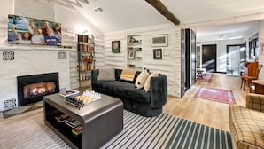 Een moderne woonkamer met een open haard, een bank, een bijzettafeltje met schaakspel en een aan de muur bevestigde televisie.