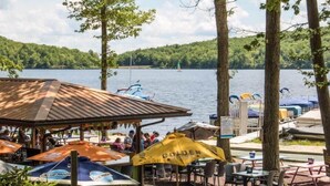 Een terras buiten met tafels en parasols, met uitzicht op een meer met bootjes.