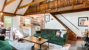 Un vaste espace de vie avec un canapé vert, un escalier en bois et une cuisine en arrière-plan.