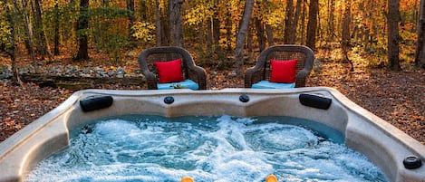 A hot tub with two chairs and a table, surrounded by a forest.