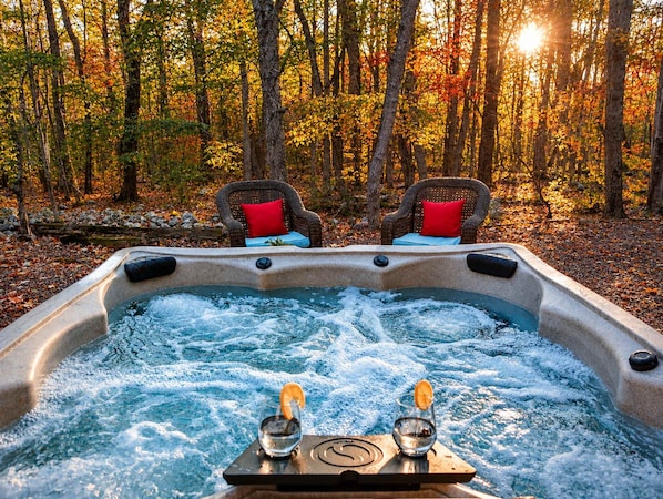 A hot tub with two chairs and a table, surrounded by a forest.
