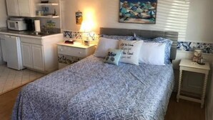 Una camera da letto con un letto, comodini, un tavolino da notte, un quadro e un angolo cottura con pensili ed elettrodomestici.