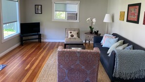 Un salon avec un téléviseur, un canapé, un fauteuil et une fenêtre.