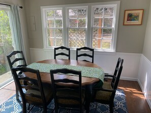 Un coin repas avec une table en bois, quatre chaises, une nappe à motifs et une fenêtre donnant sur un jardin.