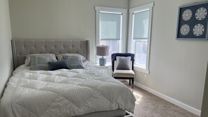 Une chambre à coucher avec un grand lit, une table de chevet, une chaise et deux fenêtres.