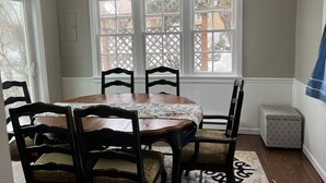 Un coin repas avec une table et des chaises en bois, une nappe à motifs et une vue par une fenêtre ornée d’un treillage.