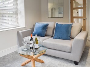 A modern living room with a grey sofa, blue cushions, a glass coffee table, and two bottles of wine.