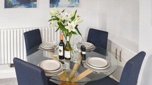 A dining table with a glass top, surrounded by chairs, set with plates, glasses, and a bottle of wine. - 2 bedroom accommodation in Silverdale (Silverdale)
