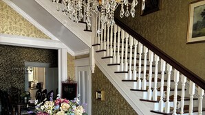 Een statige trap met witte balustrades, een kroonluchter en een ronde tafel met een bloemstuk.