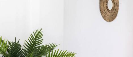 A room with a white wall, a woven wall hanging, and a potted plant with green leaves.