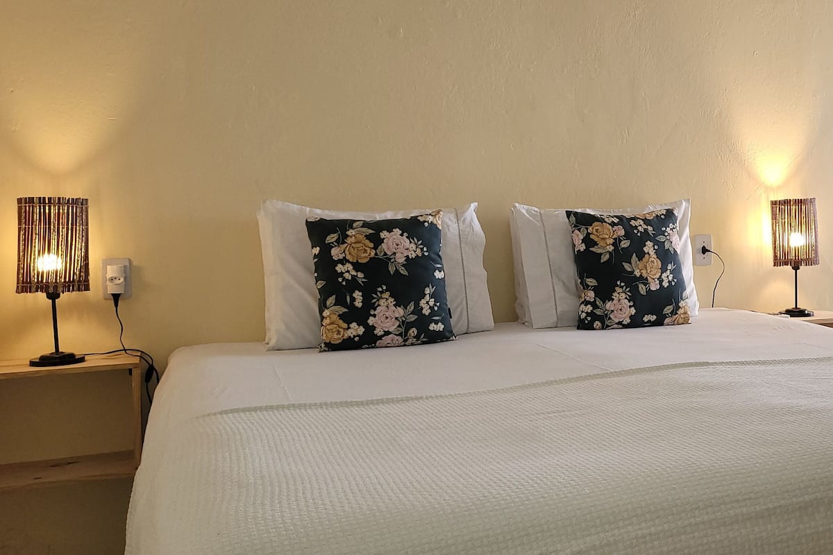 A neatly made bed with floral pillows and two bedside lamps.