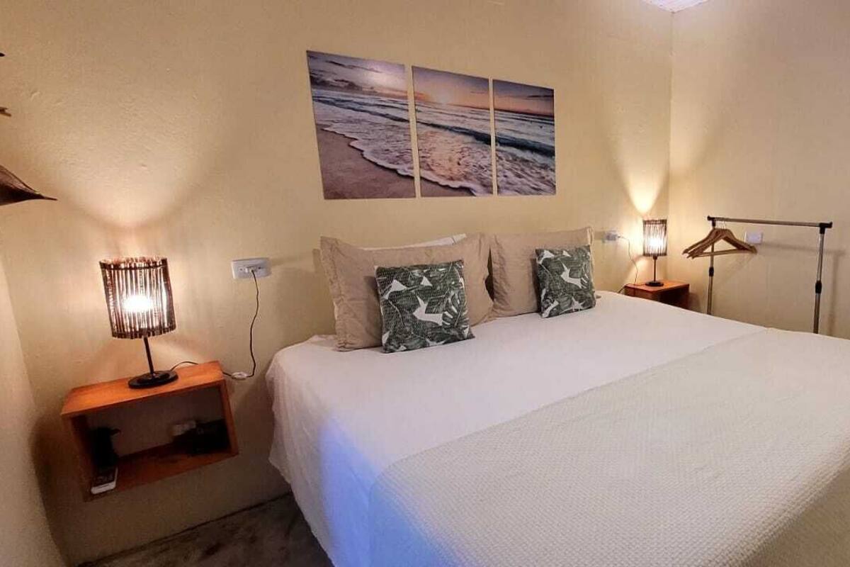 A bedroom with a bed, a nightstand, a lamp, a wall-mounted mirror, and a beach-themed wall art.