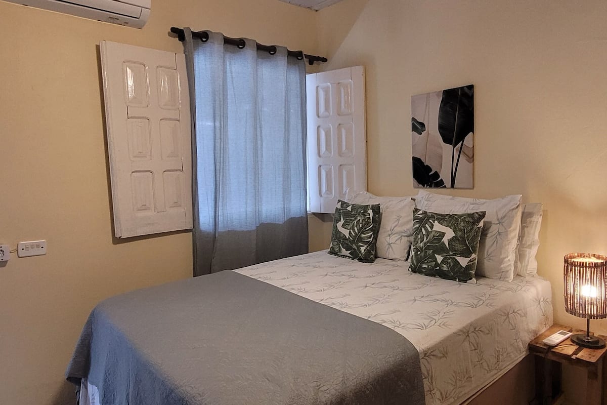 A bedroom with a bed, a nightstand, a lamp, and a door with a curtain.