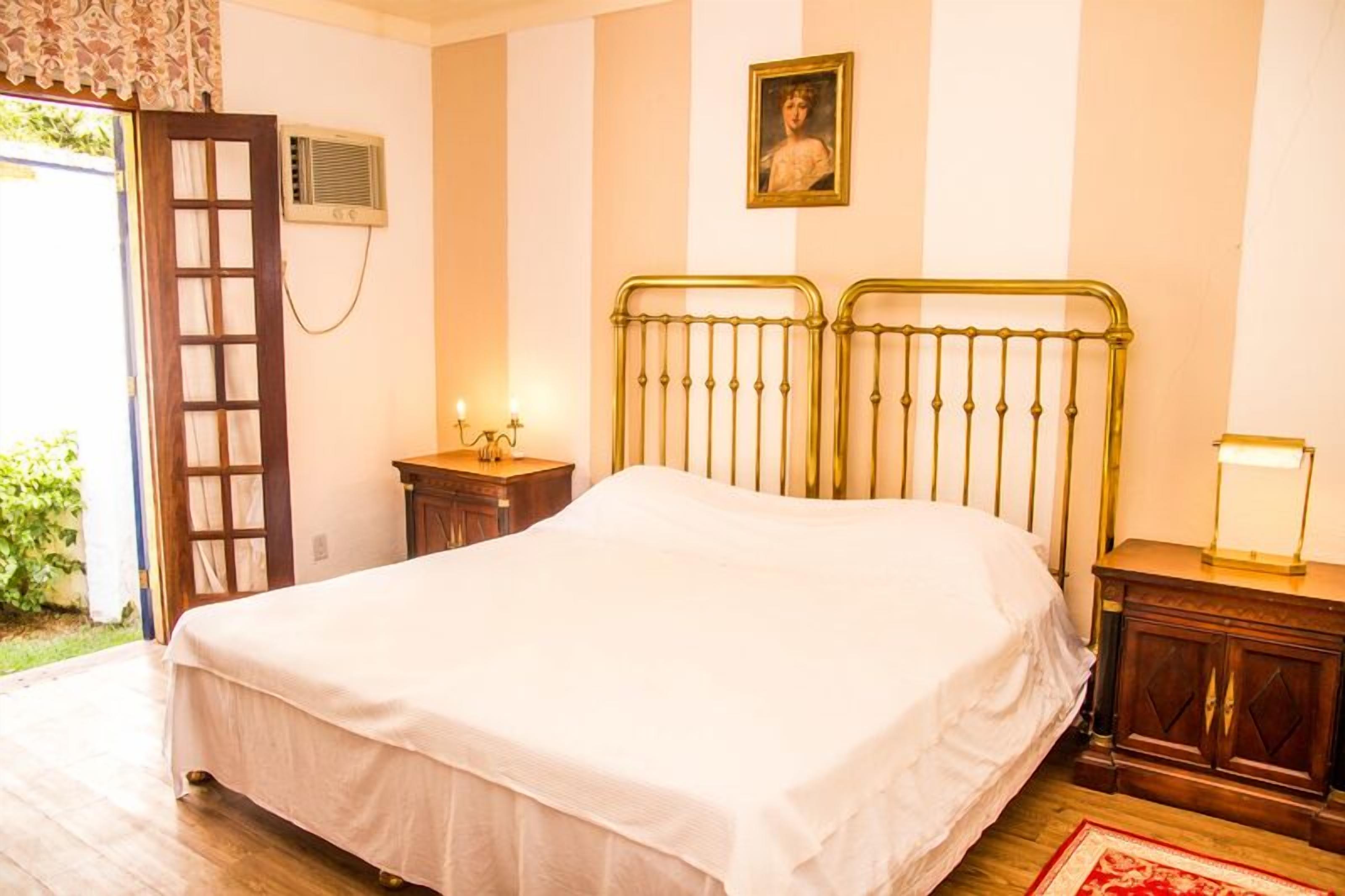 A bedroom with a bed, a nightstand, a lamp, a picture on the wall, and a window with curtains.